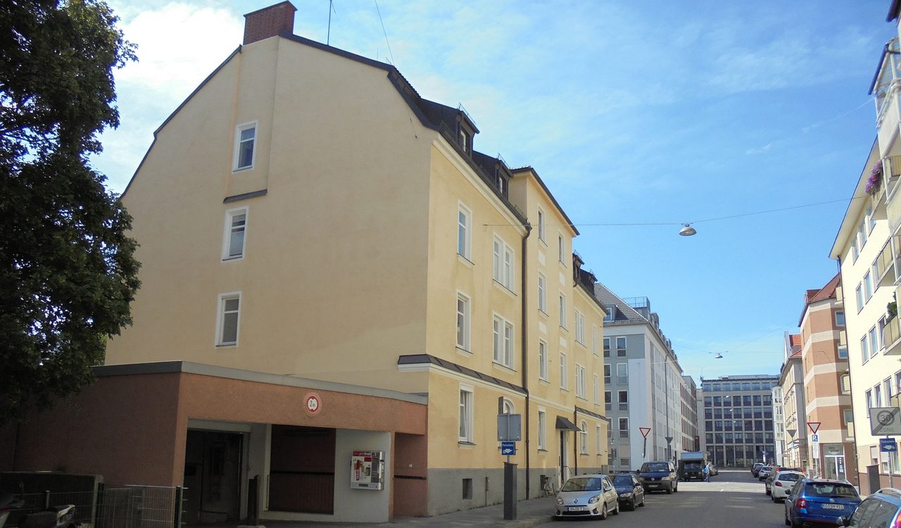 Gelbes Eckwohnhaus mit Hofdurchfahrt an einer Münchner Straßenkreuzung