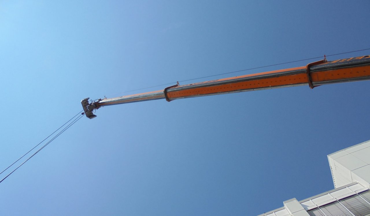 Ausleger eines Autokrans vor blauem Himmel über einem Hallendach