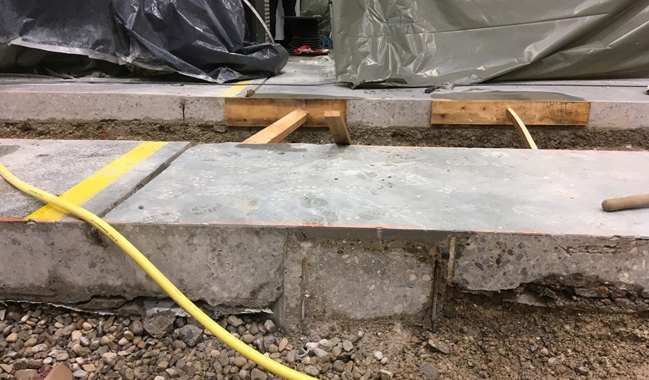 Baustellendetail: Betonplatte auf Holzkeilen über freigelegtem Fundament