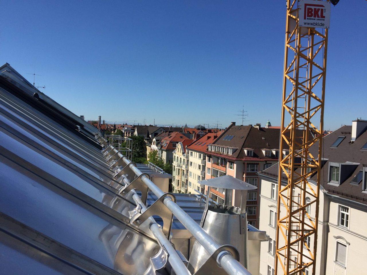 Blechabdeckung einer Dachsanierung, dahinter Münchner Wohnzeile und gelber Baukran