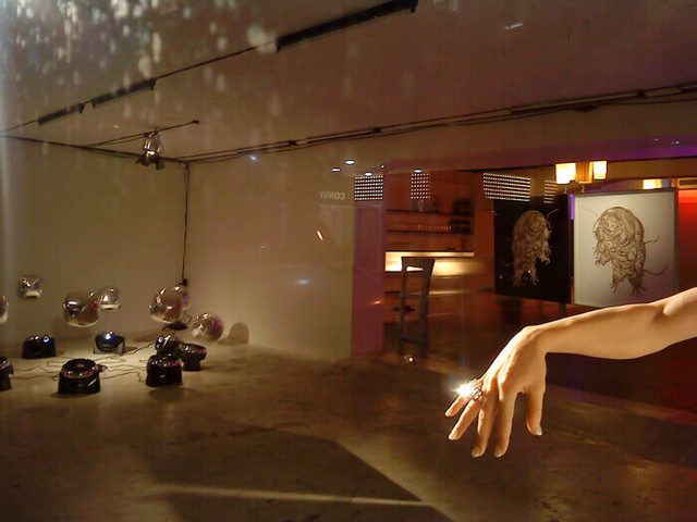 Ausstellungsraum mit Kugelobjekten am Boden und Handgrafik im warmen Licht