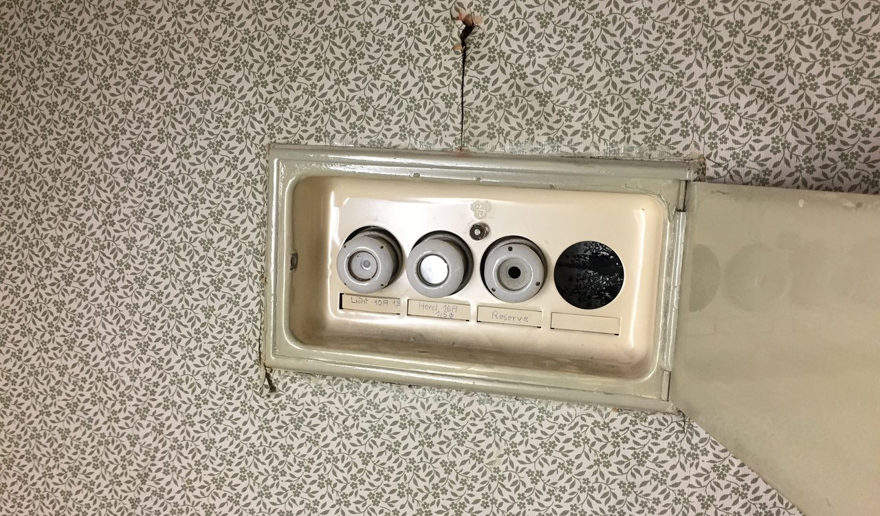 Alter Sicherungskasten auf gemusterter Tapete in einer unsanierten Wohnung