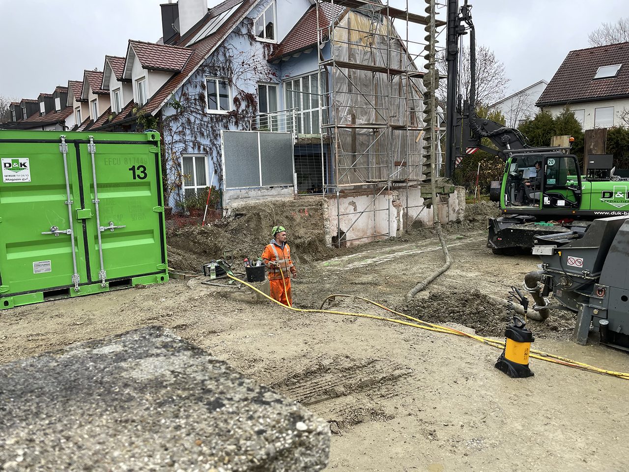 Baustelle an einem Bestandsgebäude mit Aushub, Baucontainer, Bagger und Bauarbeiter