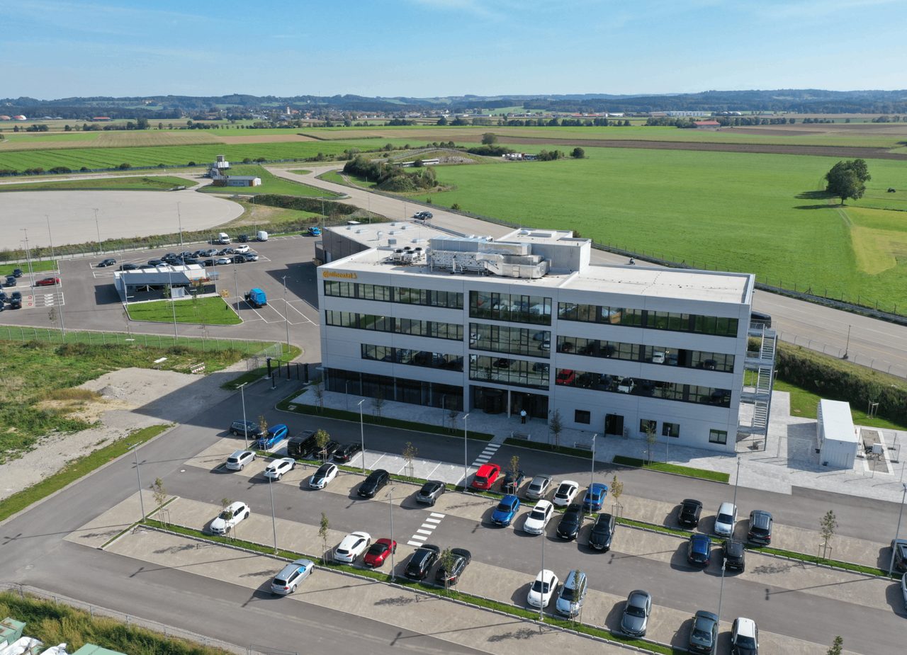Luftaufnahme eines viergeschossigen weißen Bürogebäudes mit Parkplatz zwischen Feldern